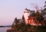 a white and red lighthouse with red brink building in the distance at sunset